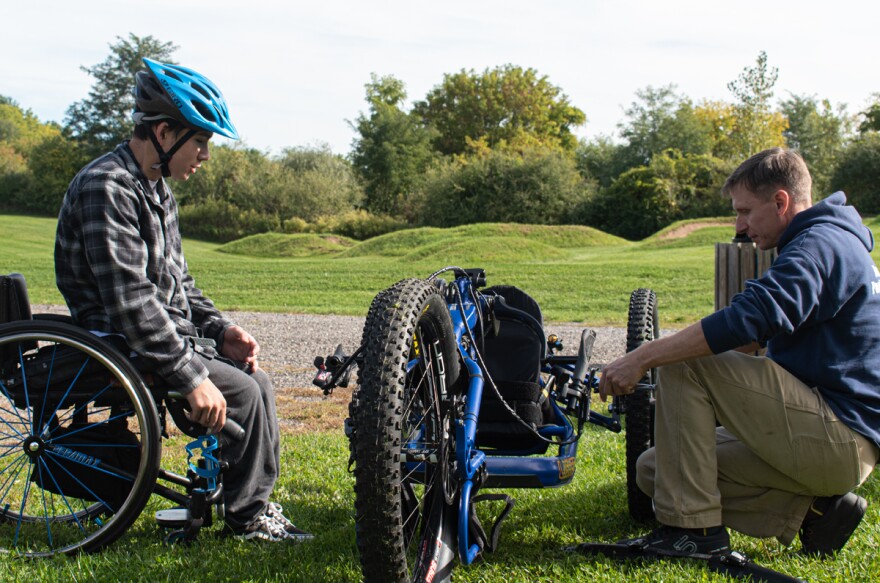 Mather Ling watches Adam Reitz, trails manager for the town of Victor, adjust an accessible mountain bike Ling is about to ride.