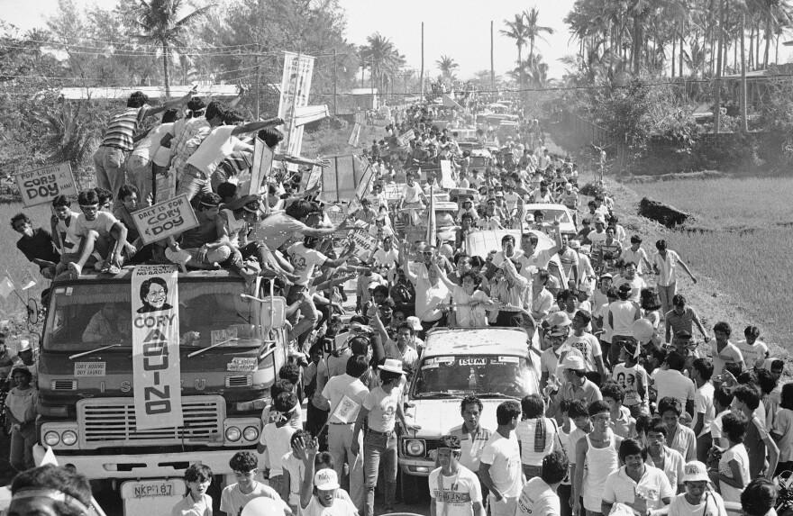 Opposition presidential candidate Corazon Cory Aquino (riding on an open truck) waves to her supporters atop a parked truck on Jan. 31, 1986, during a motorcade in this town, southeast of Manila, as she campaigned for the February 7 special presidential election, Daet, Philippines. Thousands of Filipinos greeted Mrs. Aquino and her vice presidential running mate, Salvador Laurel, during the motorcade.