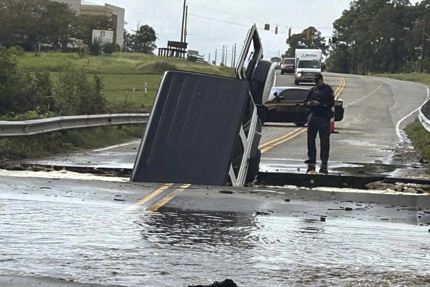 This photo provided by Brunswick County Sheriff's Office shows a police officer checking on a vehicle that fell into a sinkhole on a highway in Brunswick County, N.C., after a storm dropped historic amounts of rain, Monday, Sept. 16, 2024.