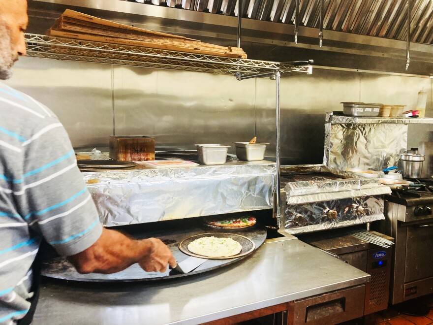  A chef uses a spatula to move pizza and naan on a spinning grill.