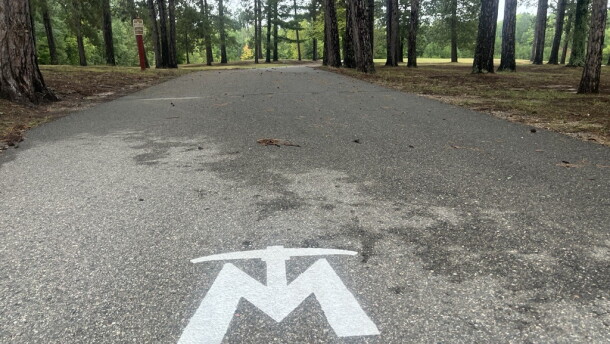 The Mesabi Trail logo is painted in white on the asphalt trail. Trees are visible in the background. 