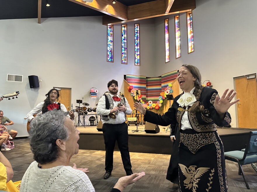 Two women sing while a band plays in the background.