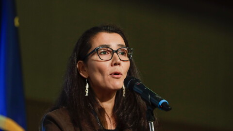 A woman in a black suit jacket speaking into a microphone.