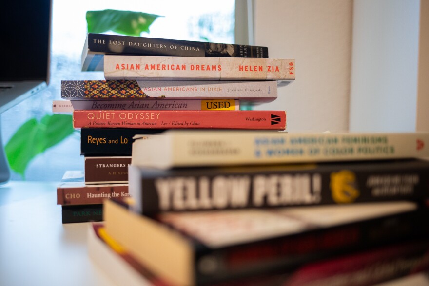 On a rainy day in Dallas, a stack of about 13 Asian American history books are photographed in front of a window. 