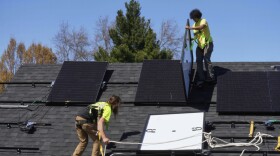 Two men install solar panels on the roof of a home.