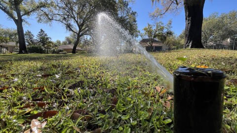 a sprinkler spraying on a lawn with trees in the background