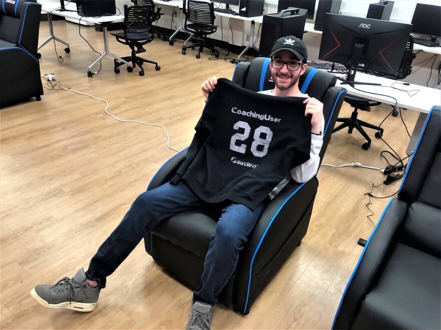 Tyler Coffman is holding an old sweatshirt he got custom-made with his gamer tag in a gaming space.