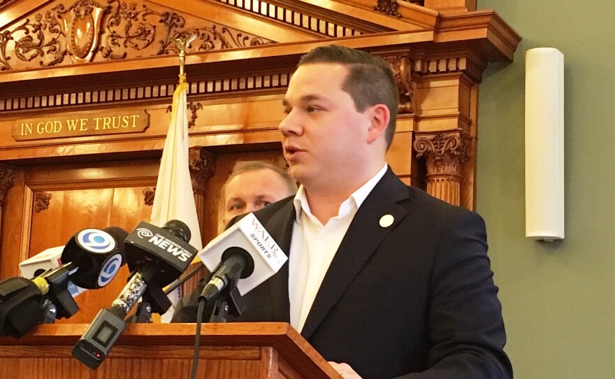 A man stands at a wooden podium looking to the left.