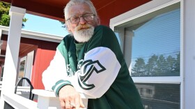 A man smoking a cigarette leans on a porch railing.