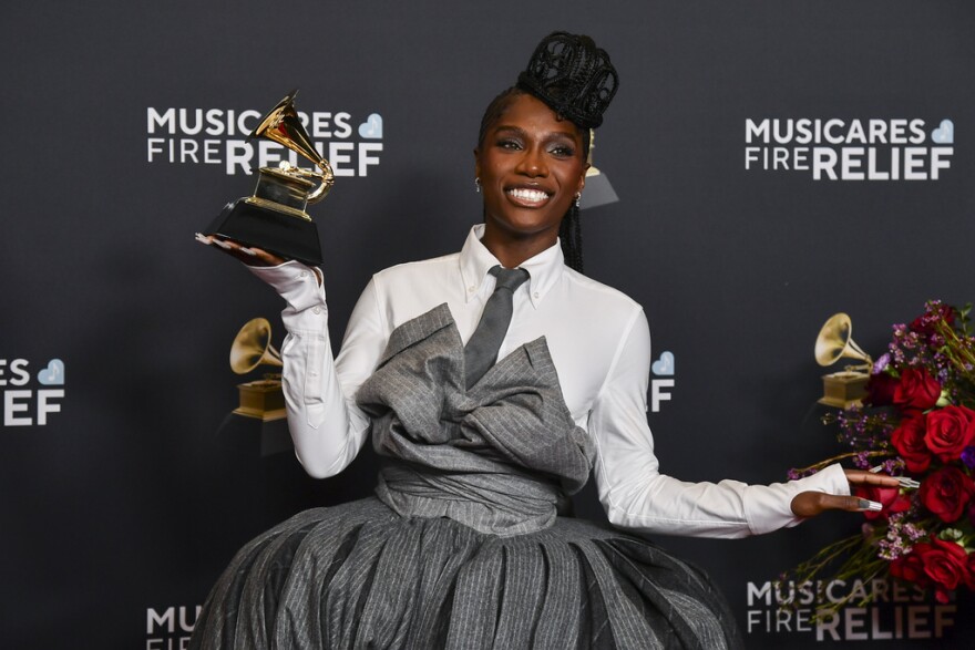 Black woman in a white dress shirt and gray tie and dress smiling and posing with a Grammy Award