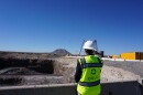 A person wearing a yellow construction vest that says "Oklo" and a hard hat is turned toward a big dirt pit.