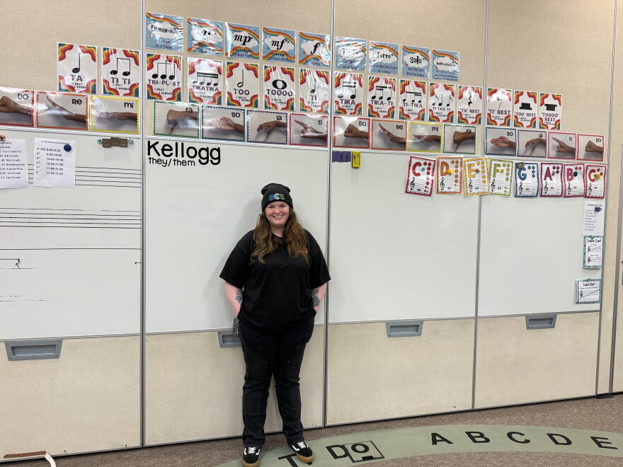 A person stands in front of a white board with music notes posted above it.
