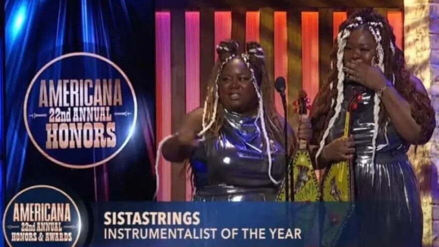 Two women accept an award on stage in a theater.