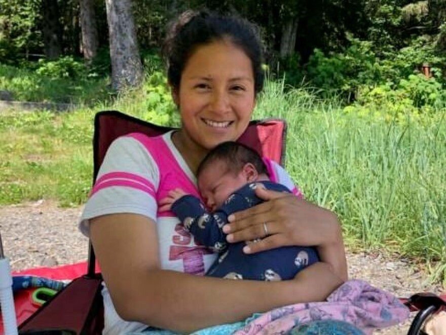 A woman sits outside in a t-shirt holding a baby.