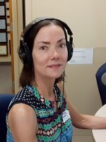 Woman wearing headphones sitting at a broadcast console.