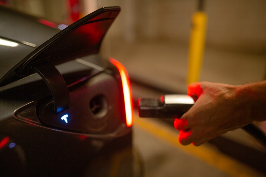 A hand unplugs a charger from a black Tesla