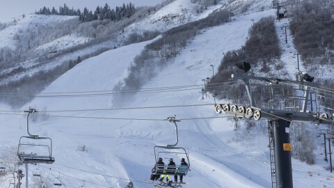 A chair lift on a mountain carries skiers up a massive hill covered in snow.