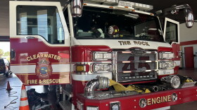 red-and-white Clearwater Fire & Rescue fire truck parked inside a fire station with its front doors open. Firefighting gear lays on the ground around.