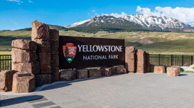 The Yellowstone National Park sign in front of large snow capped mountains.