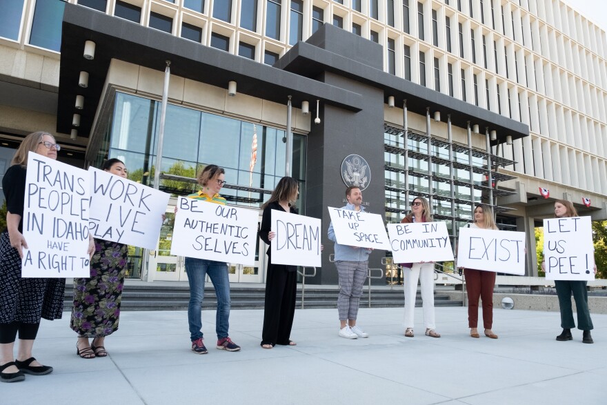 A group of people hold signs protesting a law making it a crime for transgender people to use the restroom that aligns with their gender identity.