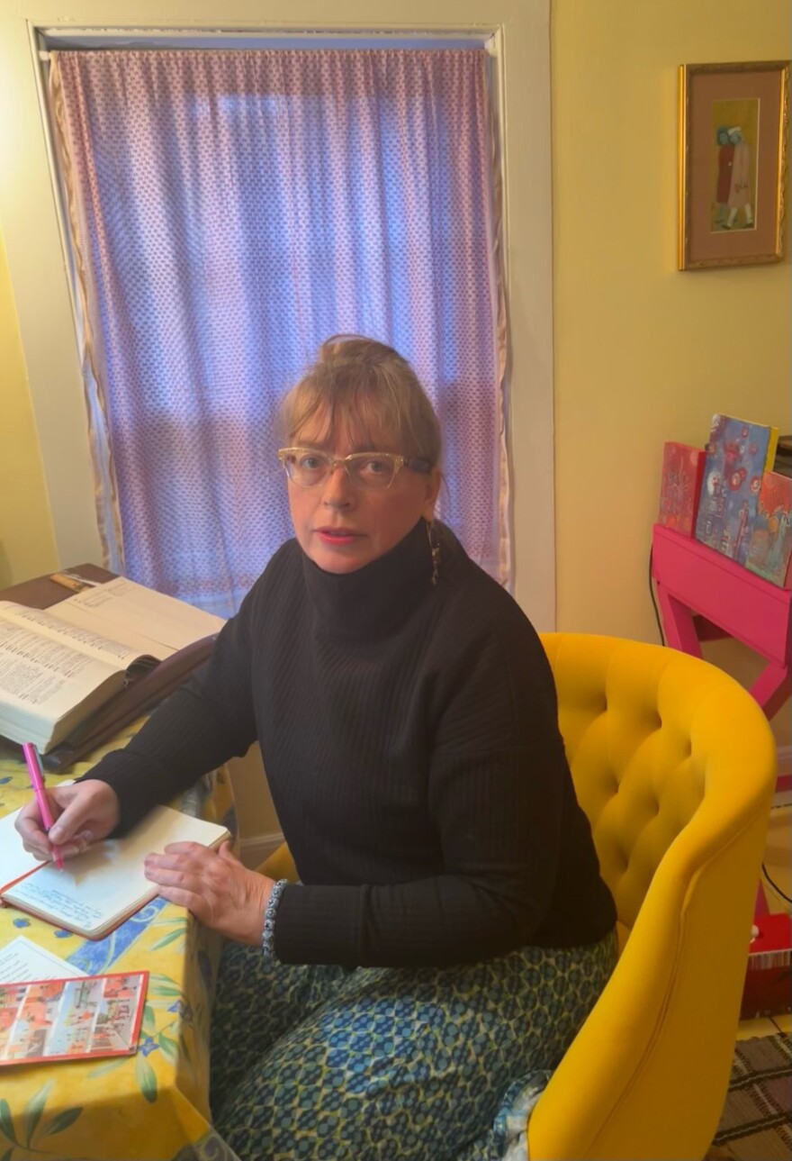 Daisy Rockwell wearing a black sweater, sitting in a yellow chair, holding a pink pen.