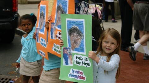 Tillie Ferguson, right, holds a poster to advertise the book she wrote for classmate Nigel Tapp, in an event to raise money for his family