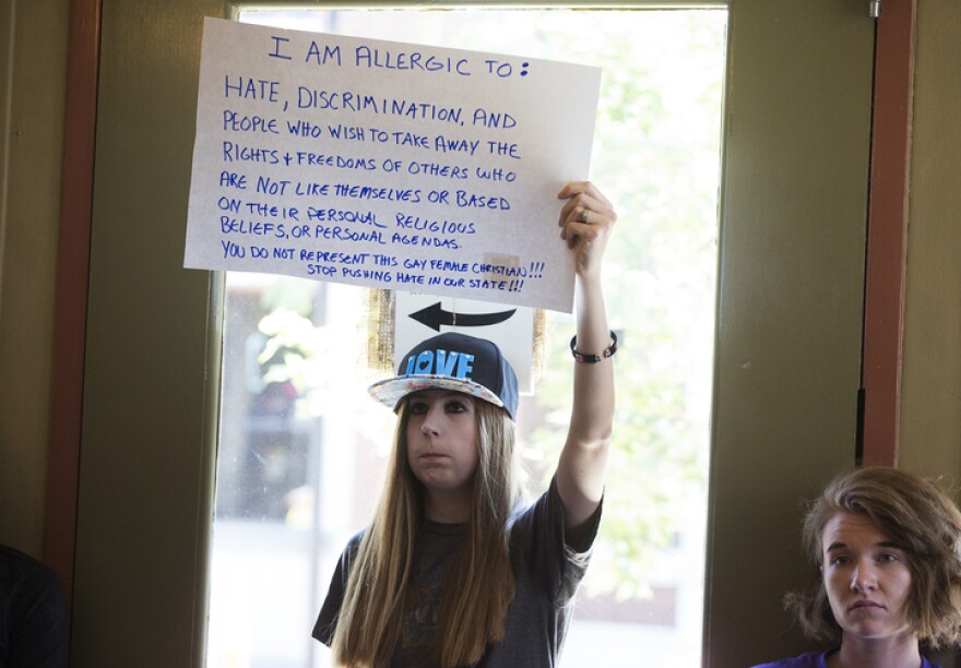 An audience member, who declined to give her full name, holds up a sign as Onder and Eigel spoke during the Politically Speaking podcast.