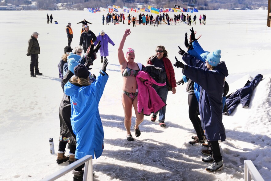 A person wearing a bathing suit walks on ice as they and other people raise their hands in celebration