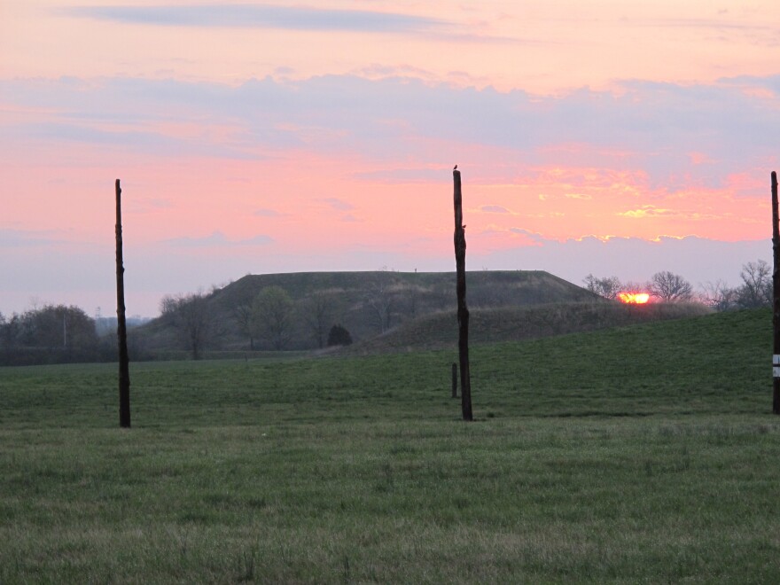 Sunrise at Monk’s Mound at Cahokia. The posts are a reconstruction of a Cahokian solstitial calendar. The circle of posts, known as Woodhenge, marked the sun’s position at the solstice.