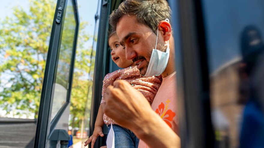 An Afghan man carries a girl as he and other refugees arrive at a processing center in Chantilly, Va., Monday, Aug. 23, 2021, after arriving on a flight at Dulles International Airport. [Andrew Harnik / AP]