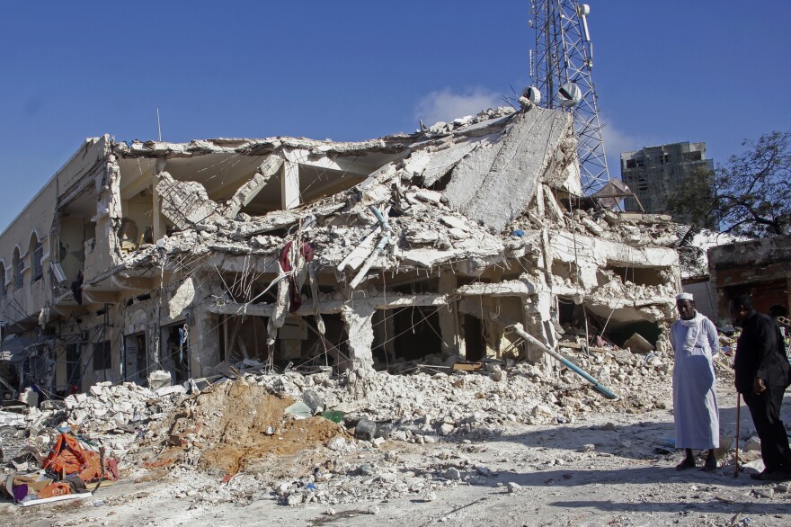 People observe a destroyed building at the scene of Saturday's double car bomb attack at a busy junction in Mogadishu, Somalia.