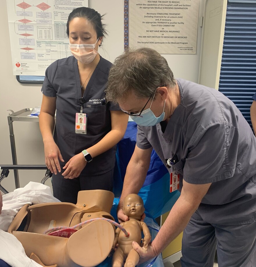 Dr. Tina Pattara-Lau and Dr. Dale McGee lean over an artificial human abdomen wearing face masks and medical uniforms.