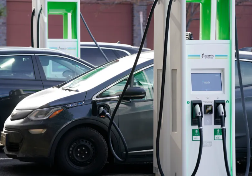 A gray car is plugged into an electric pump. Several other cars are parked as well.