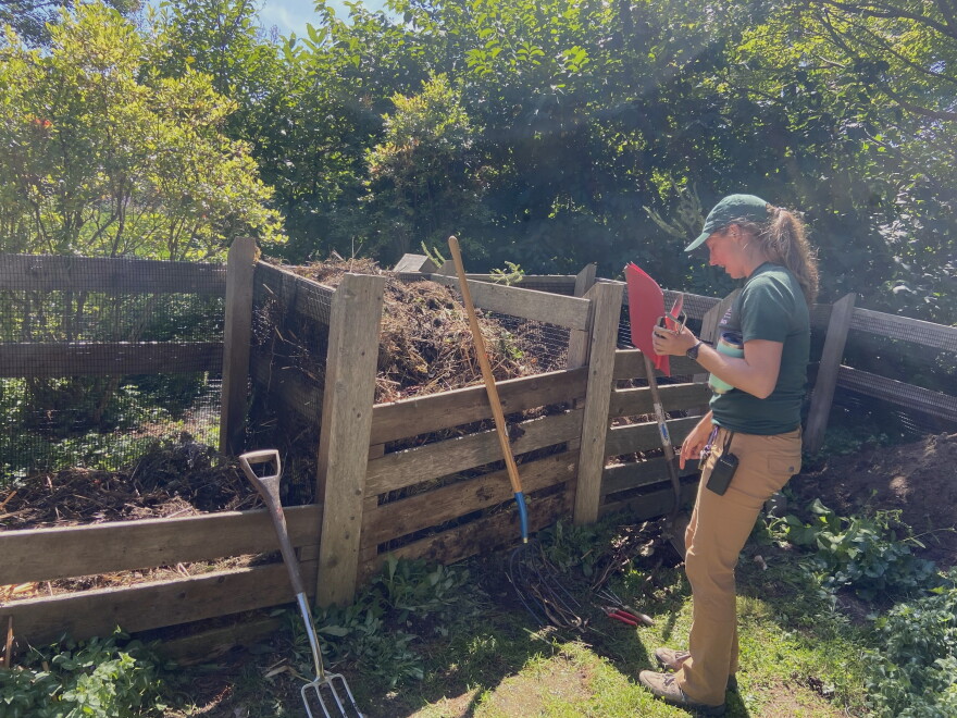 A woman stands at a compost pile.