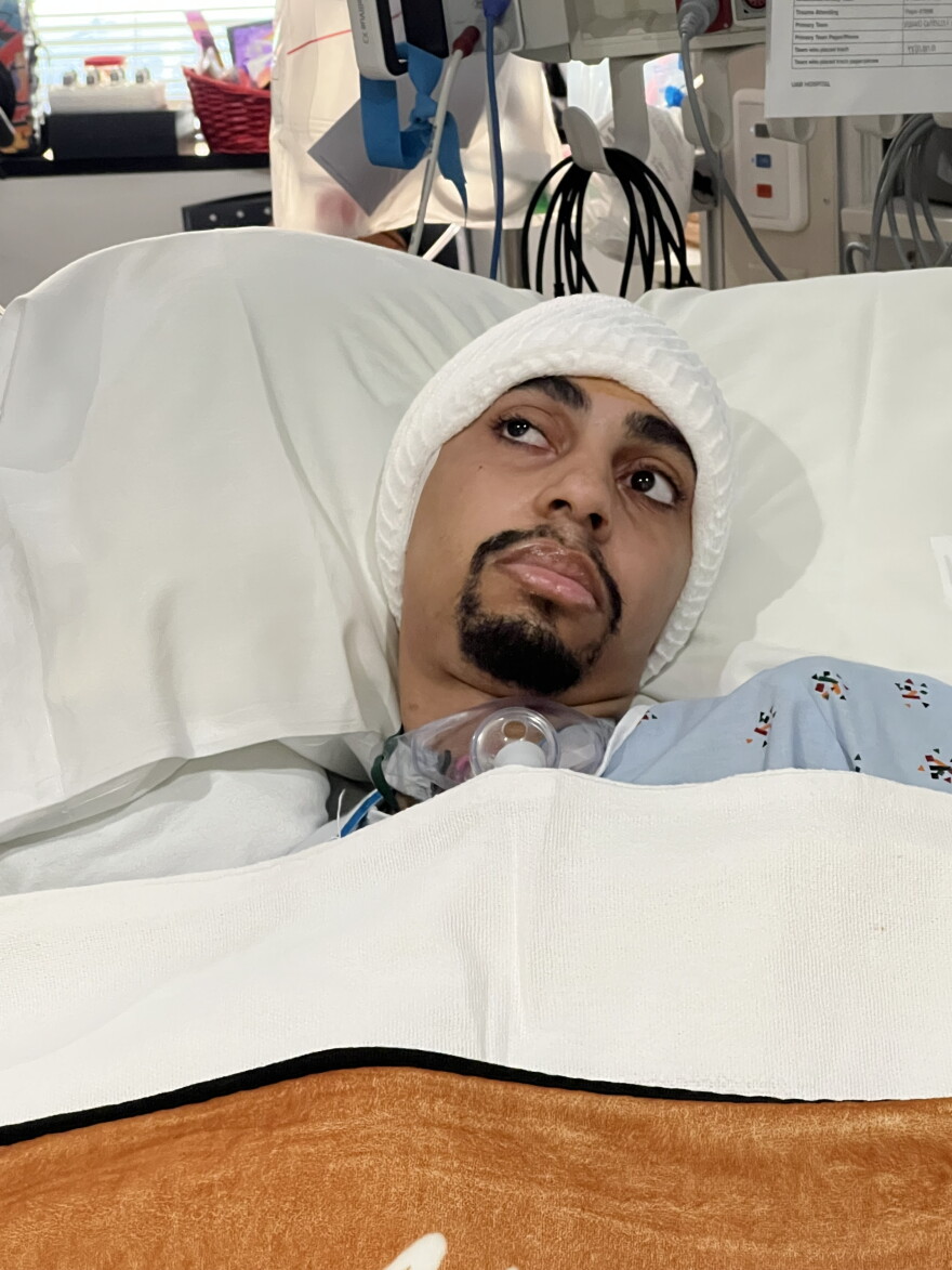 Calvin "Elijiah" Briggs lays in a hospital bed with a white hat hugging his head.