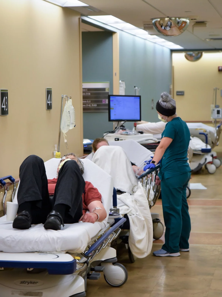 A nurse talks to a patient on a stretcher in the hallway of the emergency department at Sparrow Hospital.