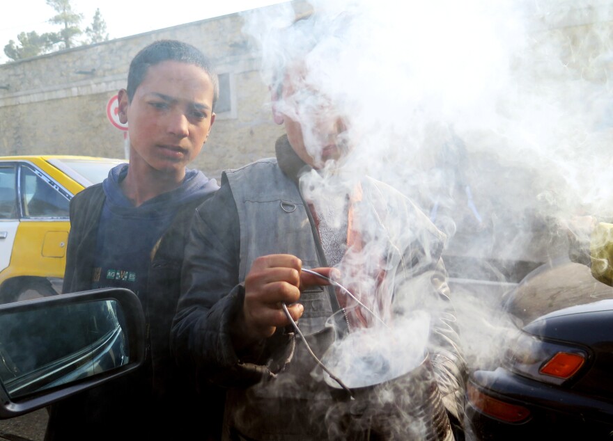 Young boys wave smoldering tin cans at cars in Kabul. The smoke from the seeds inside the cans is believed to ward off evil.