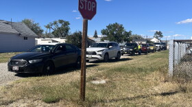 A line of cars waiting to receive food in Rock River. A stop sign in the foreground.