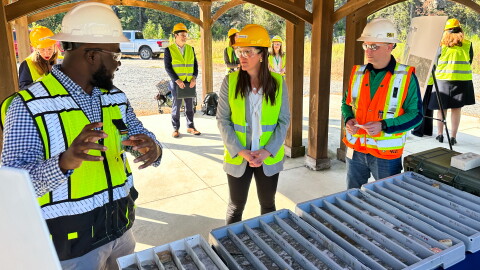 Woman and men in safety vests talk outdoors