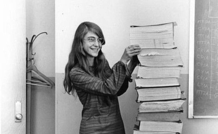woman stands beside a stack of papers