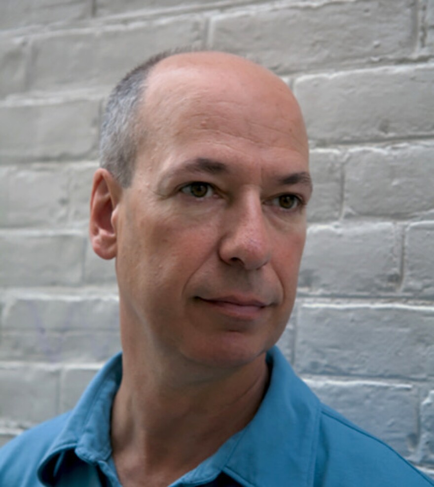 a person with short grey hair, wearing a blue, collared shirt