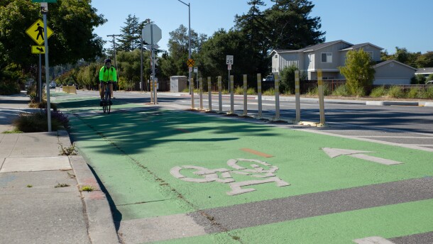 A cyclist bikes in a protected bike lane, which has dividers between the path and the main road.