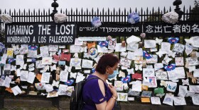 In this May 28, 2020, file photo, a woman passes a fence outside Brooklyn's Green-Wood Cemetery adorned with tributes to victims of COVID-19 in New York. The U.S. death toll from the coronavirus topped 200,000 Tuesday, Sept. 22, a figure unimaginable eight months ago when the scourge first reached the world’s richest nation with its sparkling laboratories, top-flight scientists and towering stockpiles of medicines and emergency supplies. (Mark Lennihan/AP Photo File)