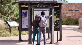 Two people facing away from the camera are looking at a sign of the national park map.