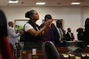 Rep. Carla Cunningham wears a black vest over a white short-sleeve shirt. Her hair is braided and in a bun. She is clapping, surrounded by other clapping lawmakers on the House floor.