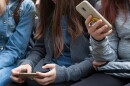 Two young teenage girls sitting holding smartphones in their hands.