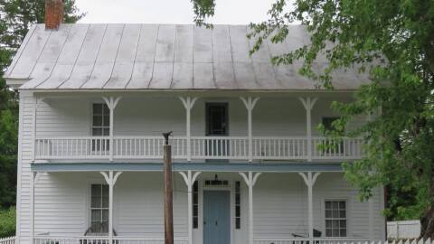 A white two-story building with a large porch and a white picket fence. 