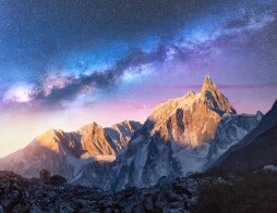 Milky Way over beautiful mountains at night in Nepal. Colorful space landscape with purple starry sky, snowy mountain peak and sunlight at sunrise. Galaxy, stars and high rocks. Travel and nature