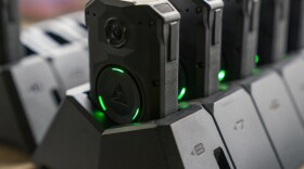 Black police body cameras lined up in charging stations.