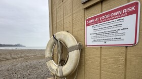 A life ring hangs on a hook on the side of a shed at Edgewater Beach. A sign hangs next to it, which reads, "Swim at your own risk."